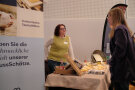 Eine Frau steht hinter einem Infostand und unterhält sich mit einer Teilnehmerin.